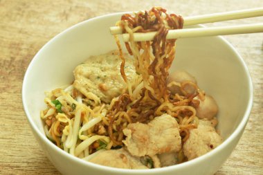 Çubuklar kuru sarı yumurtalı erişte topluyor. Dilimlenmiş domuz eti ve kasede köfte var.