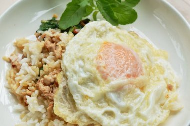 spicy fried chop pork with basil leaf and chili topping egg on rice in dish