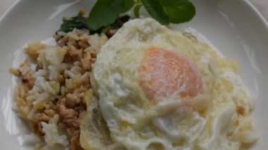spoon scooping creamy egg yolk topping spicy fried chop pork with basil leaf and chili on rice in dish