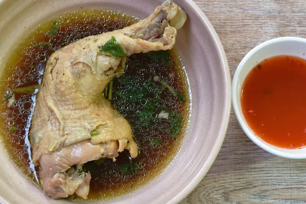 boiled chicken thigh and leg with herb brown soup in bowl dipping spicy chili sauce cup