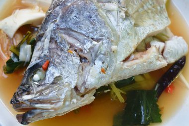 Baharatlı levrek balığı kafası ve hindistan cevizi dilimi tabakta Tom Yum çorbası.