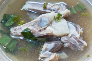 Kaynamış domuz kemiği, şeffaf çorbada, kasede masada.