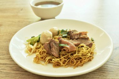 Çin usulü sarı erişteli domuz eti ve tabakta kemik ve kahverengi bitki çorbası fincanı.