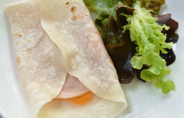 Berrito doldurulmuş jambon, peynirli ve soslu domuz eti. Tabakta birkaç taze sebze ye.