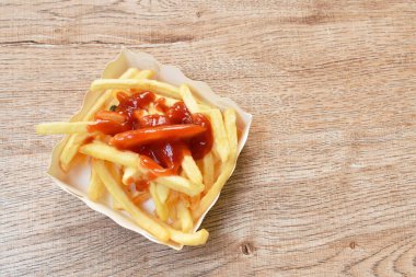 Patates kızartması karton kutuda tuzla karıştırılmış masaya ketçap bandırılmış.