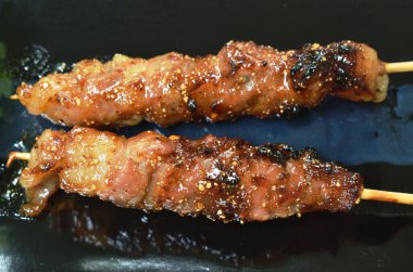  Baharatlı soslu ızgara domuz sarması, ahşap sopaya saplanmış ve tabağında sebze var.