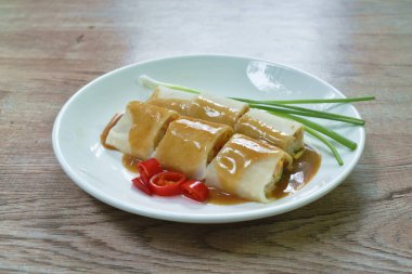  Un ambalajlı Çin böreği ve fasulye filizi soslu domuz eti. Tabakta kırmızı sos var.