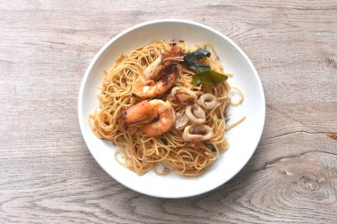 spicy fried vegetarian Chinese yellow rice noodles with shrimp and squid couple chili basil on plate