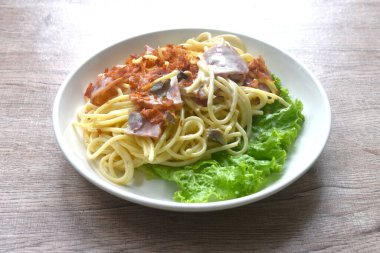 Kızarmış spagetti beyaz lahana krema sosu dilimlenmiş domuz pastırması ve tabakta marul. 