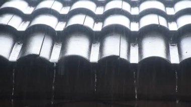 Evdeki kiremit çatısına şiddetli yağmur yağıyor ve yere düşüyor.