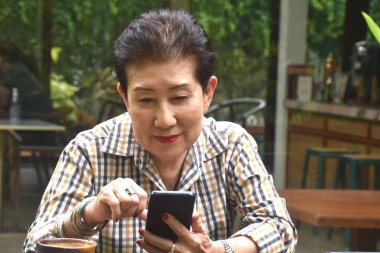 Yaşlı kadın kahve içmekten, kitap okumaktan ve kafede cep telefonu kullanmaktan hoşlanıyor.