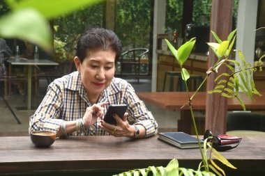 Yaşlı kadın kahve içmekten, kitap okumaktan ve kafede cep telefonu kullanmaktan hoşlanıyor.