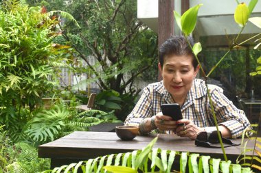 Yaşlı kadın kahve içmekten, kitap okumaktan ve kafede cep telefonu kullanmaktan hoşlanıyor.