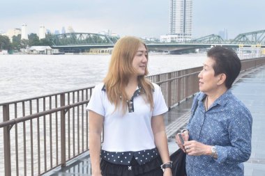 Asyalı yaşlı kadın ve kızı, yağmurlu bir günde Tayland 'da Cho the nehrinin manzarası ile konuşmaktan zevk alırlar.