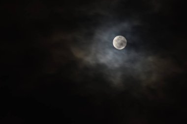 Geceleyin gökyüzünde bulutlarla kaplı dolunay.