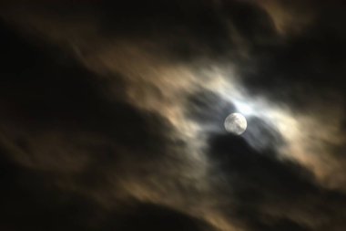 Geceleyin gökyüzünde bulutlarla kaplı dolunay.