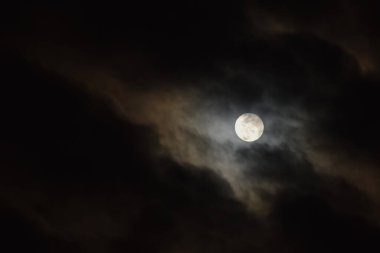 Geceleyin gökyüzünde bulutlarla kaplı dolunay.