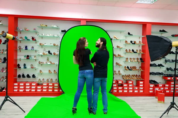 Couple stand on the green screen in the shoes store. There\'s a blank space for ad content on their t-shirt. Chromakey - technology of combining two images. Brand\'s position. Latin guy and european girl. Relationship, racial equality and diversity.