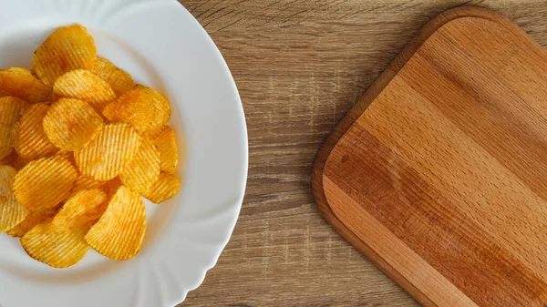 Beyaz bir tabakta patates cipsi ve boş alanı olan bir kesme tahtası.