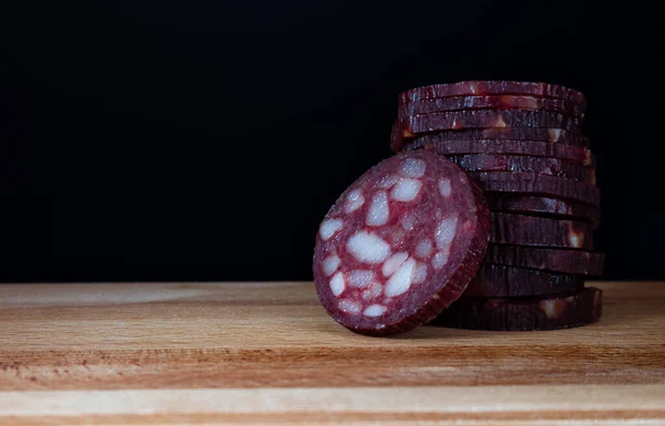 Chopped dry sausage close-up on wooden board and black background