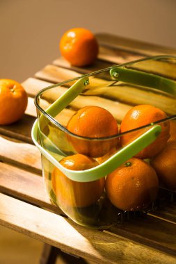 Fresh Oranges in a Clear Basket on a Rustic Wooden Table, Fresh tangerines in a metal basket on a wooden table.