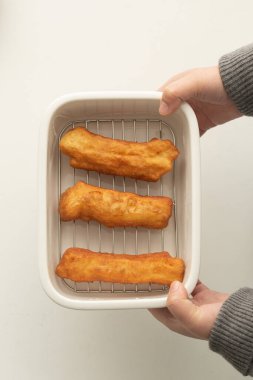Ellerinde taze kızarmış Youtiao tepsisi, Vietnam hamur çubukları, beyaz arka planda beyaz plastik bir kapta kızarmış peynir çubukları.