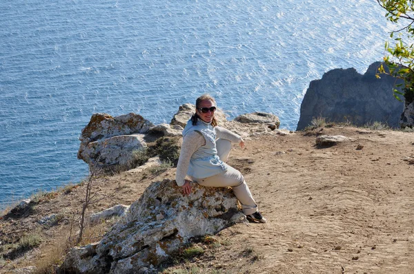 Woman in sunglasses sitting on a rock — Stock Photo, Image