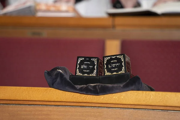 A pair of tefillin on a synagogue bench, the name of Jerusalem written in hebrew on their casings.