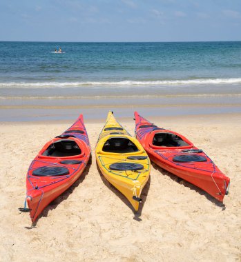 Güneşli bir günde kumlu bir sahilde üç renkli kano. Arka planda sakin bir deniz.