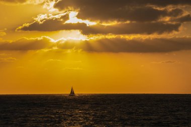 Güneş ufka doğru batarken denizde bir yelkenli..