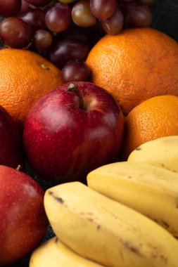 Üç üzüm, mandalina, muz ve elma, siyah bir tencerede.