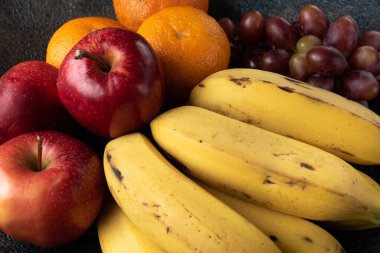 Üç üzüm, mandalina, muz ve elma, siyah bir tencerede.