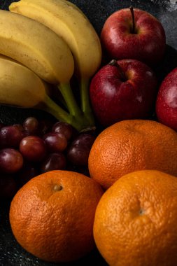 Üç üzüm, mandalina, muz ve elma, siyah bir tencerede.