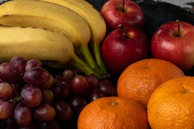 Üç üzüm, mandalina, muz ve elma, siyah bir tencerede.