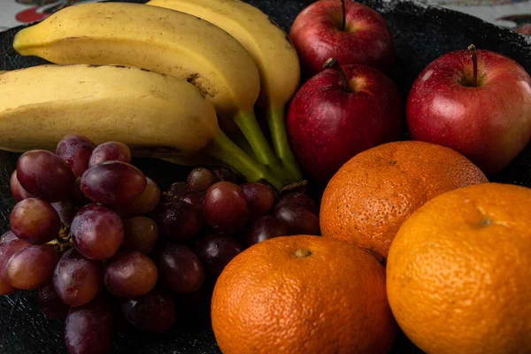 Üç üzüm, mandalina, muz ve elma, siyah bir tencerede.