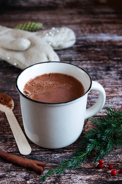 Weiße Tasse heißen Kakao oder Schokolade auf einer rustikalen Holzplatte mit Zimt, Tannenzweigen, Strickhandschuhen im Hintergrund. — Stockfoto