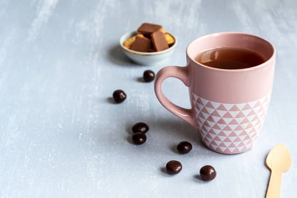 Rosa Tasse schwarzer Tee auf grauem Hintergrund, mit Keksen, Pralinen und einem Holzlöffel. Kopierraum. — Stockfoto