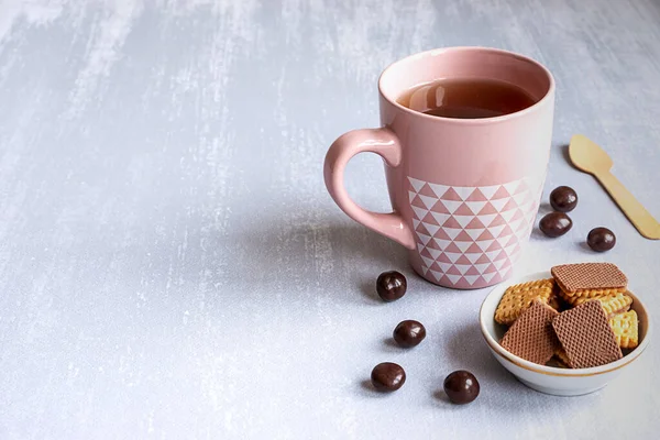 Rosa Tasse schwarzer Tee auf grauem Hintergrund, mit Keksen, Pralinen und einem Holzlöffel. Kopierraum. — Stockfoto