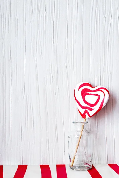 Hartvormige lolly in een glazen pot tegen lichtgrijze ondergrond, op rood-witte tafel, Valentijnsdag concept, kopieerruimte — Stockfoto