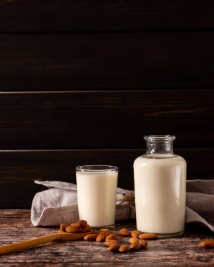 Bir şişe ve bir bardak badem sütü, koyu renkli ahşap arka planda, fotokopi alanı ile