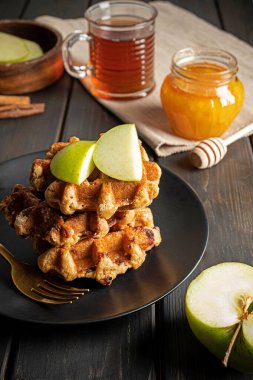 Geleneksel Belçika waffleları dilimlenmiş yeşil elma, bal ve kahvaltıda bir fincan çay. Koyu ahşap arkaplanda kompozisyon.