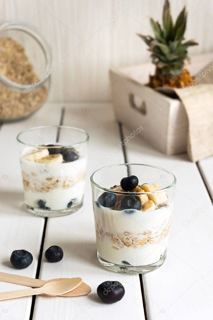 Two glasses with layered yogurt, oats and fruits, on white wooden table. Healthy breakfast, healthy lifestyle concept