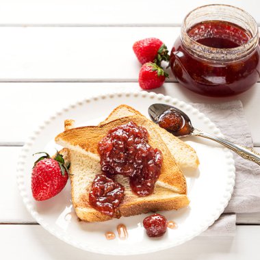 Toasted bread slices with strawberry jam and a jar of jam