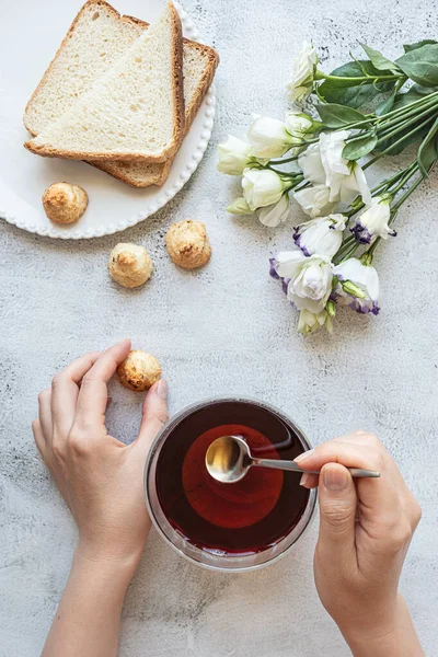 Vista superior de uma mulher mãos com uma xícara de chá, biscoitos, pão torrado e flores — Fotografia de Stock