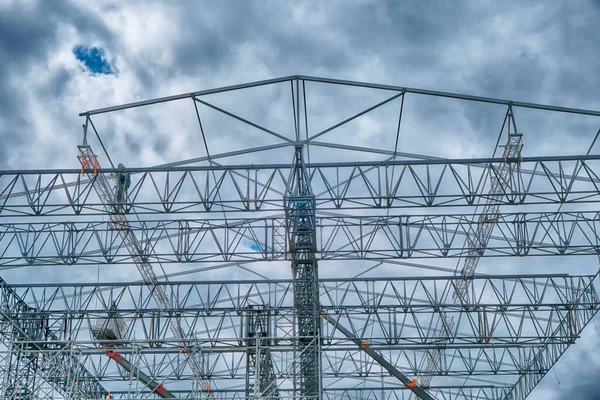 Workers build large metal structures for the concert stage. Cloudy sky with thunderclouds