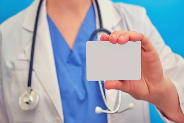 A woman doctor holds a blank business card, close-up. A nurse in medical dress with a small blank form, copy space for text on a blue background