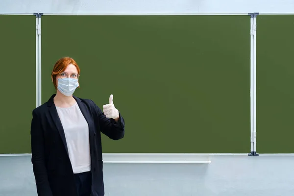 Concept for quarantine removal in school after the coronavirus epidemic. Teacher opens class after pandemic in medical mask and protective gloves, copy space for text