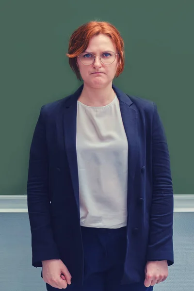 Portrait of a young teacher with a sad face near school blackboard