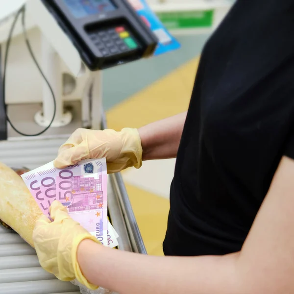 Woman hands in protective gloves count money at the cash register of the store. Euros in the customer hands of a supermarket