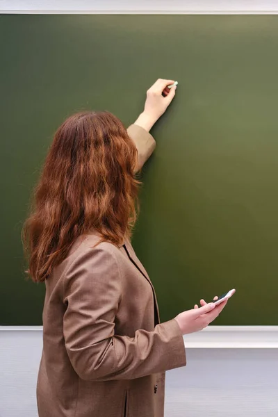 Woman teacher writes a text in chalk on a school blackboard